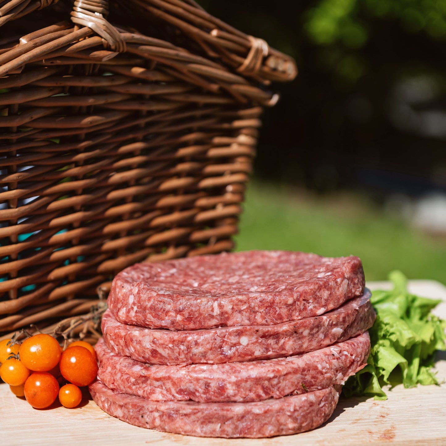 Glebe Farm 6oz Beef Burgers on a wooden board with a wicker basket and vegetables in the background.