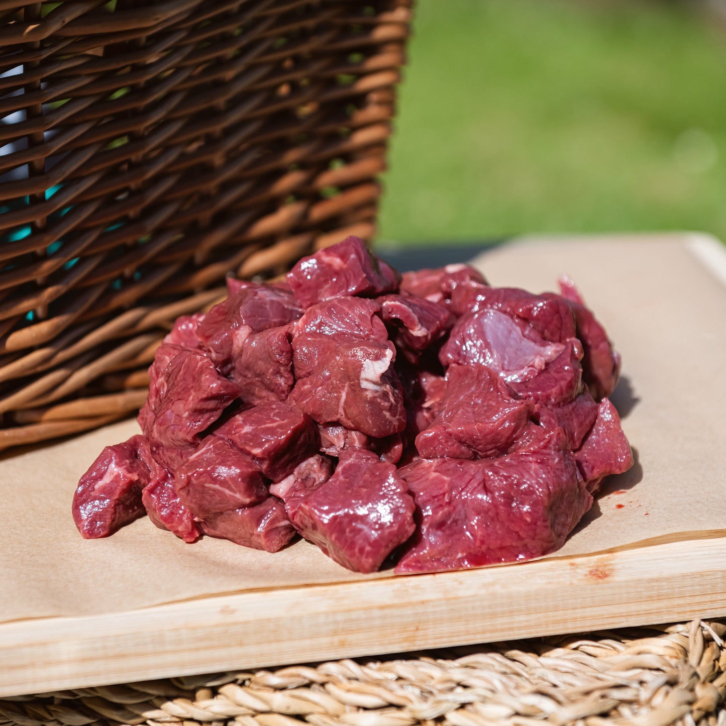 Glebe Farm Beef Steak Pieces on a wooden cutting board with a wicker basket in the background.