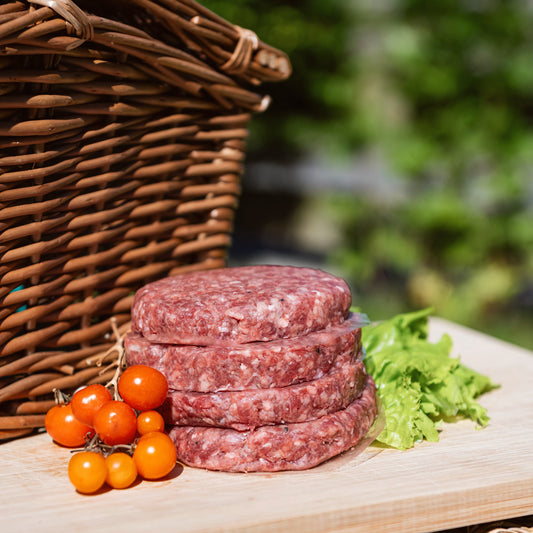 Stack of burgers on a wooden board with a wicker basket and vegetables in the background