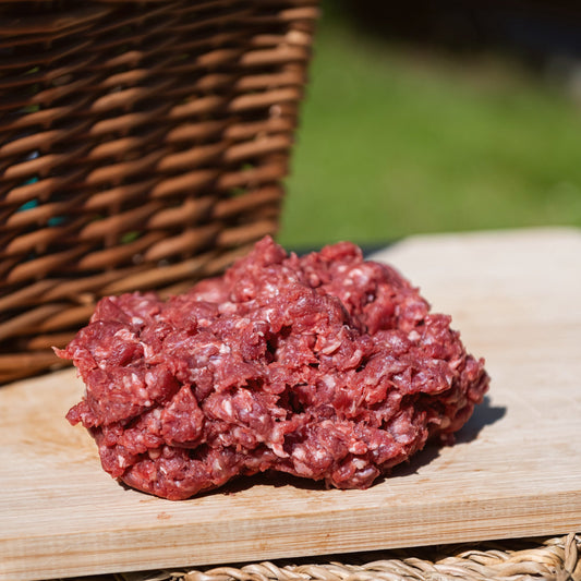 Glebe Farm Beef Mince on a wooden cutting board with a wicker basket in the background.