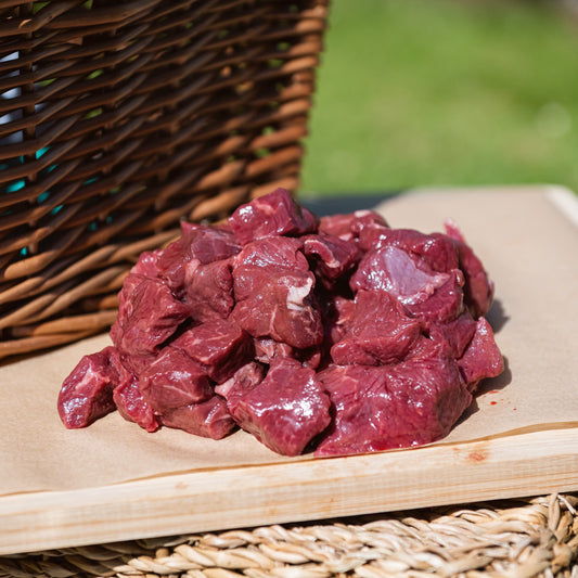 Glebe Farm Beef Steak Pieces  on a wooden cutting board with a wicker basket in the background.