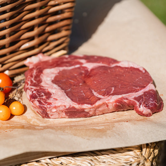 Glebe Farm Ribeye Steaks  on a wooden cutting board with berries and a wicker basket in the background.
