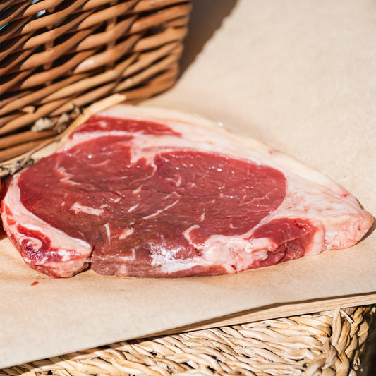 Glebe Farm Sirloin Steaks on a wooden surface with tomatoes and a basket in the background